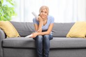 Une femme assise sur son canapé tient un téléphone fixe et fait une grimace