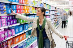 Une femme choisit un paquet de serviettes dans un rayon de supermarché