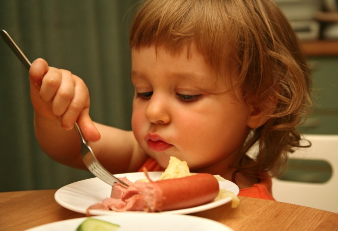 Une petite fille devant une assiette de saucisses de Strasbourg