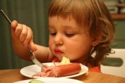 Une petite fille devant une assiette de saucisses de Strasbourg
