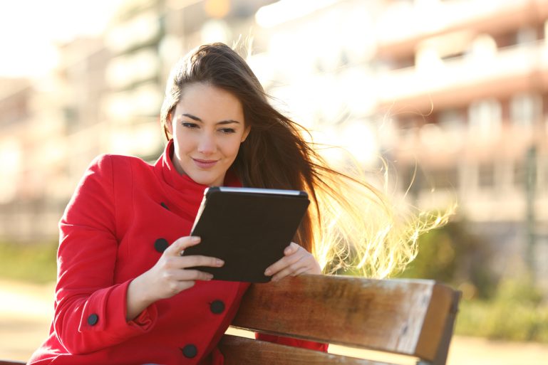 Une femme lit sur sa tablette en extérieur
