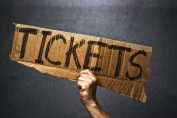 Une main brandit un carton avec le moto "tickets" écrit dessus