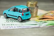Une voiture miniature devant une pile de pièces et de billets en euro