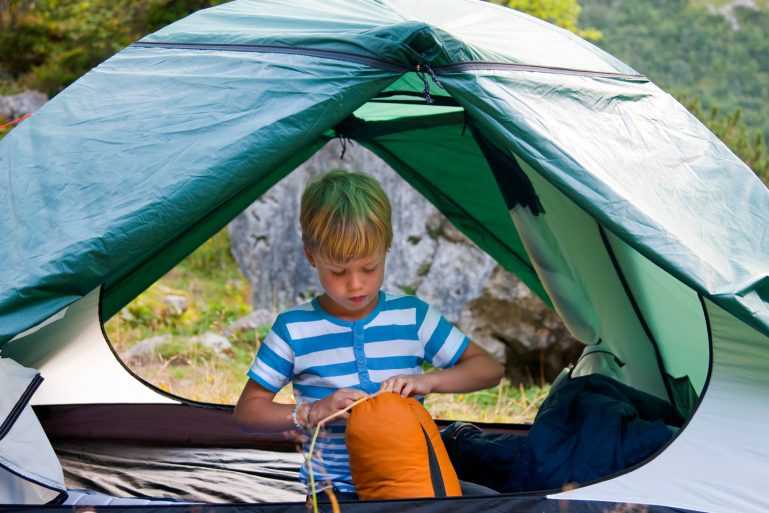 dans une tente, un garçon range son sac de couchage