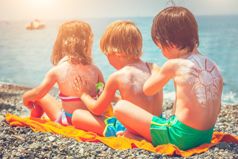 Trois enfants se passent de la crème solaire dans le dos