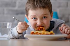 Un petit garçon mange des lasagnes