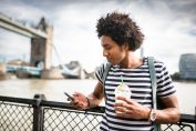 Un jeune homme regarde son smartphone avec le London Bridge en arrière plan