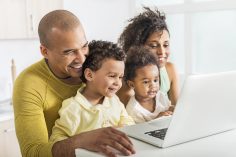 un couple regarde l'écran d'un portable avec ses deux enfants sur les genoux.