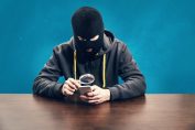 Un homme cagoulé observe un téléphone à la loupe