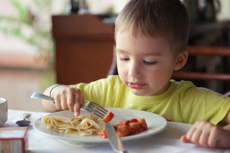 Un jeune garçon mange un saucisse knack avec des spaghettis