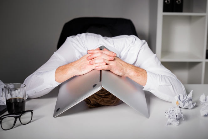 Un homme la tête sous son ordinateur portable