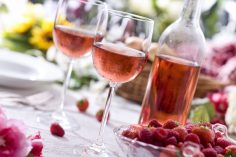 Une bouteille de rosé, deux verres servis et une assiette de framboises