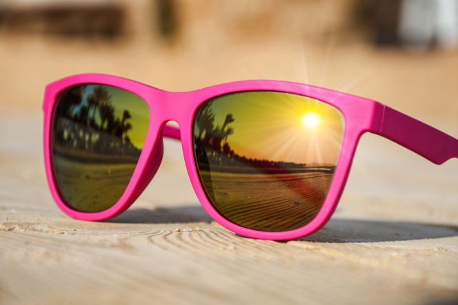 Une paire de lunettes de soleil roses sur laquelle vient se refléter le coucher de soleil.