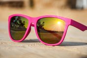 Une paire de lunettes de soleil roses sur laquelle vient se refléter le coucher de soleil.