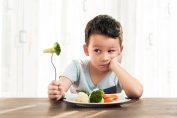enfant essayant de manger des brocolis et des carottes