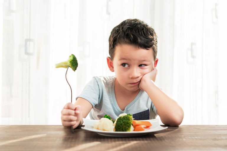 enfant essayant de manger des brocolis et des carottes