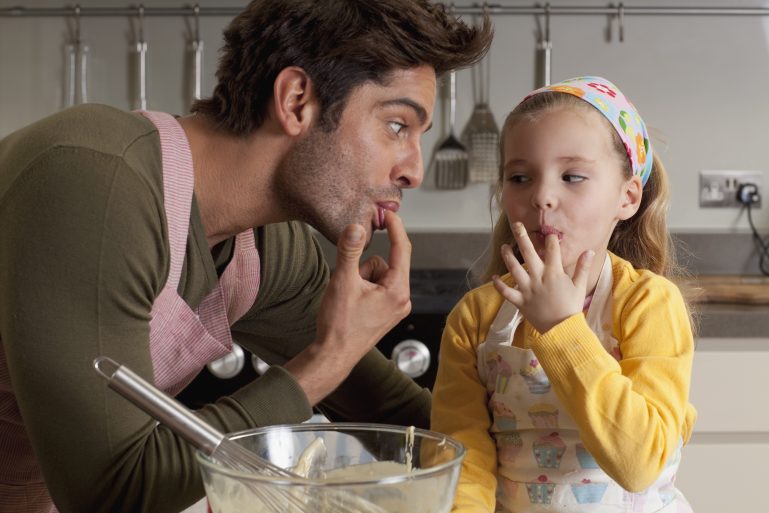 Un père et sa fille goûtent dans la cuisine de la pâte qu'ils viennent de préparer