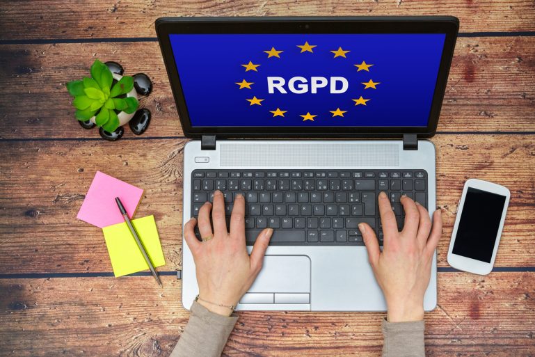 Une femme tape sur le clavier d'un ordinateur, devant un écran affichant le logo de l'europe et les lettres RGPD