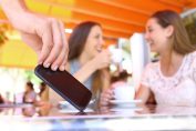 Deux femmes discutent en fond. Au premier plan, une main d’homme subtilise un smartphone.