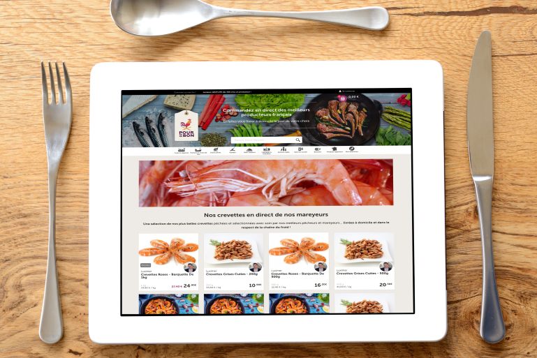 Une tablette présentée comme une assiette avec les couverts. En fond, une appli de livraison de produits frais.. 
