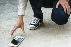 Un homme ramasse un smartphone dont l’écran est cassé