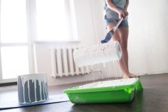 Une femme fait couler le trop plein de peinture blanche de son rouleau.