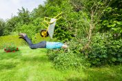 Dans un jardin, un homme saute dans un buisson