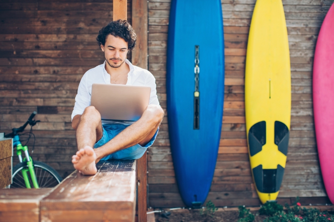 Un homme avec son ordinateur devant des planches de surf