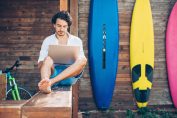 Un homme avec son ordinateur devant des planches de surf