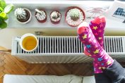 Vue du dessus d’un chauffage sur lequel sont posés une tasse de thé et des pieds croisés chaussés de chaussettes multicolores.