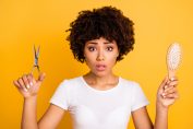 Une jeune femme avec des cheveux crépus tient des ciseaux et une brosse à cheveux