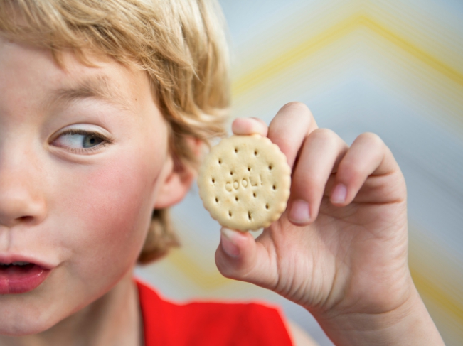 Un jeune garçon tient un biscuit à son oreille à la manière dun coquillage 