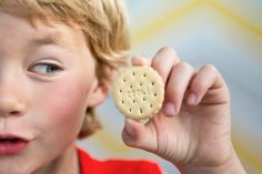 Un jeune garçon tient un biscuit à son oreille à la manière dun coquillage