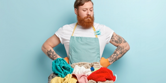 Un homme avec un air dubitatif regarde un bidon de lessive et un panier de linge