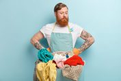 Un homme avec un air dubitatif regarde un bidon de lessive et un panier de linge