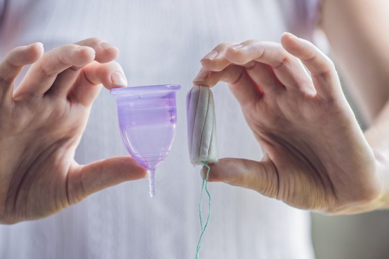 Une femme tient une coupe menstruelle et un tampon dans ses mains