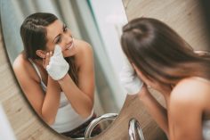 Une femme se démaquille avec un gant devant son miroir
