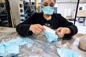 Dans une usine, une femme emballe des masques de protection dans un sachet.