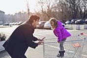un papa avec sa fille dans un chariot de supermarché