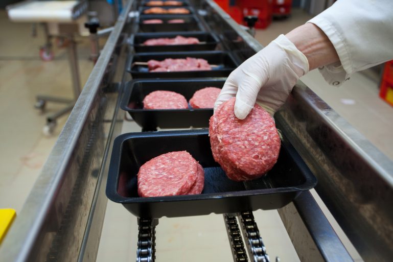 Des barquettes de viande hachée sur une chaîne dans une usine