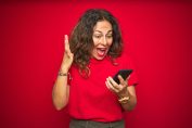 Une femme sur un fond rouge crie en regardant son téléphone mobile