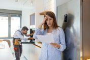 Un plombier en arrière plan et une femme catastrophée avec une facture à la main