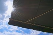 Un store noir déroulé avec ciel bleu et soleil en arrière-plan