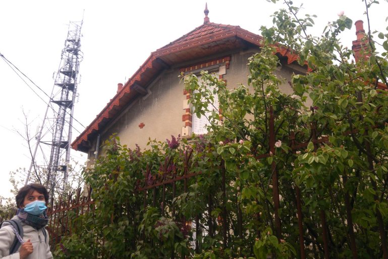 Une femme devant une maison avec en arrière plan une antenne-relais