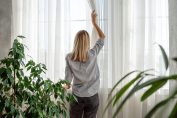 Une femme ouvre les voilages blancs de sa fenêtre