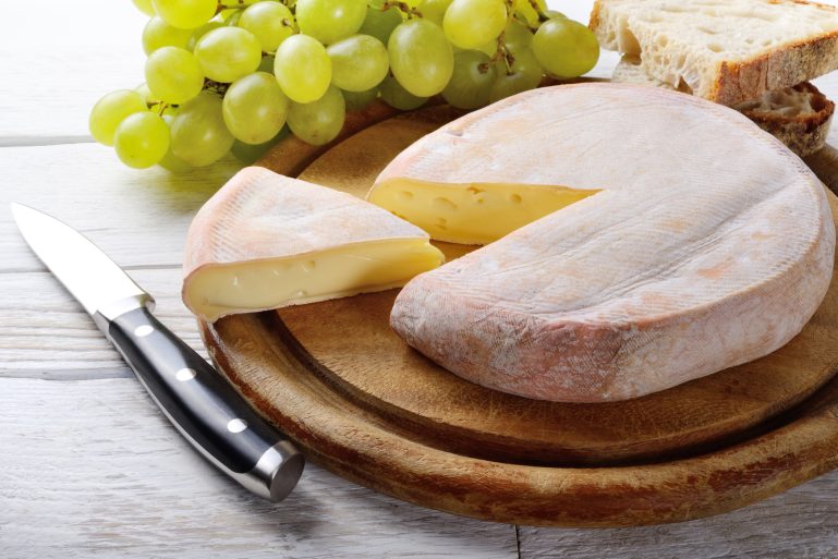un reblochon posé sur une planche avec une grappe de raisin