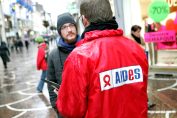 Un homme avec un anorak aux couleurs de l'association Aides démarche une personne dans la rue