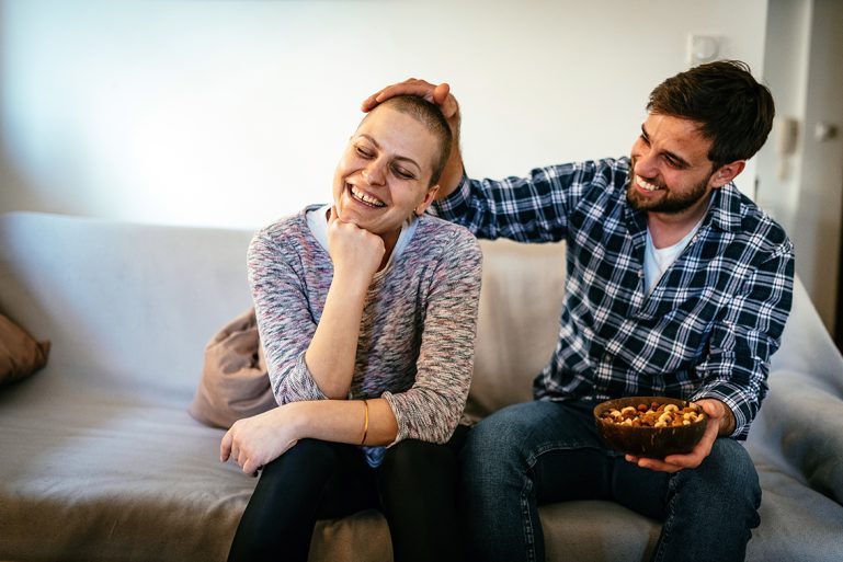 Un couple assis sur un canapé ; la femme a subi une chimiothérapie et a les cheveux qui repoussent