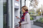Une femme avec sa carte bancaire devant un distributeur de billets