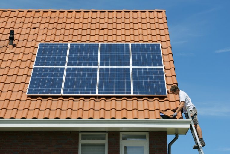 Un artisan termine l'installation de panneaux solaires sur un toit.